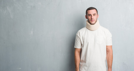 Young caucasian man injured over grey grunge wall wearing neck collar with a confident expression on smart face thinking serious