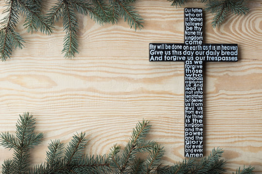 Black wooden cross with the Lord's prayer on the shabby wooden plank with fir tree branches background