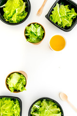 Healthy fast food concept. Light meal with lettuce in plastic containers near wooden spoons and green tea on white background top view space for text