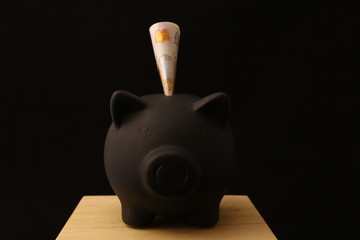 Saving money - black piggy banks with 10 pounds on black background with lightings - obrazy, fototapety, plakaty