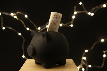 Saving money - black piggy banks with 10 pounds on black background with lightings