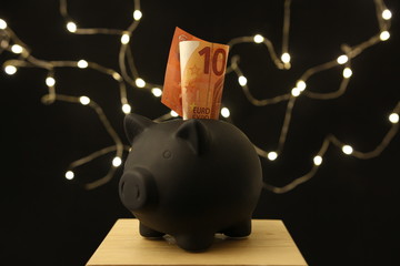 Oszczędzanie - czarna świnka skarbonka z banknotem 10 euro na ciemnym tle - obrazy, fototapety, plakaty