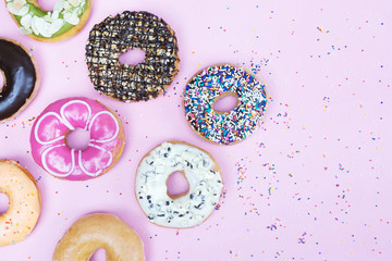 assorted donuts with chocolate frosting, topping sprinkles donuts Colorful variety and Variety of flavors mix of multi colored sweet donuts with frosted sprinkled on pink background. top view
