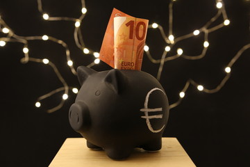 Saving money - black piggy banks with 10 EURO on black background with lightings - obrazy, fototapety, plakaty