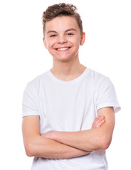 Fototapeta premium Half-length emotional portrait of caucasian teen boy wearing white t-shirt. Funny teenager with arms folded, isolated on white background. Handsome child looking at camera.