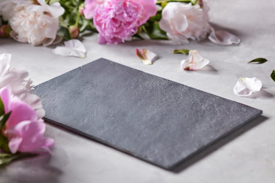 Fototapeta Petals and flowers of pink peonies on a gray concrete background with a black slate board and copy space for the dough. Postcard