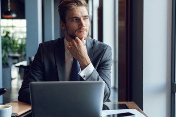 Attractive businessman using a laptop and smiling while working in cafe