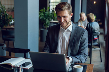 Attractive businessman using a laptop and smiling while working in cafe