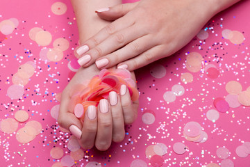 Obraz na płótnie Canvas Beautiful young woman's hands on pink pastel background with festive multi color confetti.