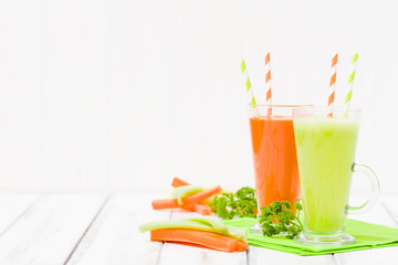 Carrot and celery juice with fresh vegetables on bark plates on wooden background.