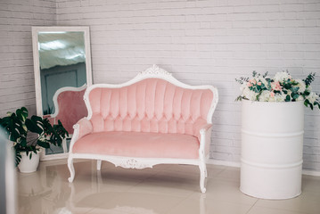 Pink sofa against the background of a white brick wall. Mirror and barrel. The scenery in the interior.