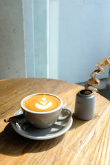 A cup of cafe latte coffee in gray ceramic cup with cinnamon and dried plant on wooden table in a cafe on blurred background