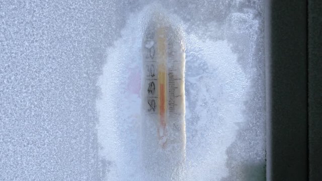 Thermometer behind frozen window at extreme cold winter day