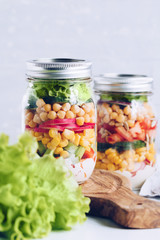 Glass jars with layering vegan salad for lunch or dinner. The concept of fitness, healthy lifestyle and vegetarian food.