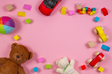 Baby kids toys frame with teddy bear, wooden toy car, colorful bricks on pink background. Top view