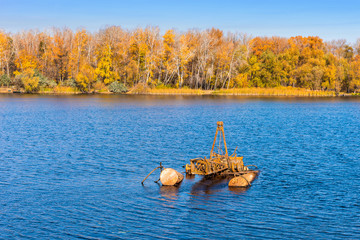 Autumn landscape - coastline with trees with yellow leaves and rusty metal construction in water