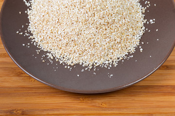 Uncooked fine-ground barley groat on brown dish close-up