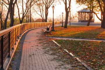 Fototapeta na wymiar Alley with fence, benches and street lights in autumn park