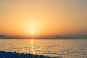 Aerial view of tropical beach on sunrise with straw umbrellas. People walk on the beach early morning