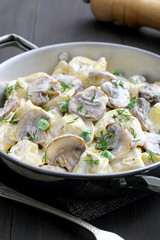 tortellini ripieni con panna ,funghi e piselli,in tegame di metallo su sfondo grigio