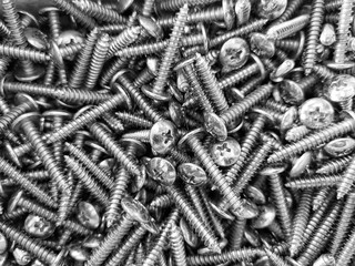 Closeup image of Many silver wood screw, flat head, spiral and tipped lay on the floor. Black and White Image