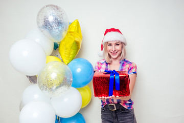 Fototapeta na wymiar portrait of young Beautyful blondу amazed woman with christmas box gift on red background. lady in a plaid shirt and santa claus hold a bag full of presents near helium multi-colored balloons studio