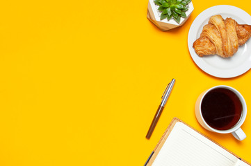 Cup of coffee, open notebook with blank pages, fresh croissant, cactuses succulents on yellow blue minimalistic background, top view Flat Lay with copy space. Empty office desk, Still life, business