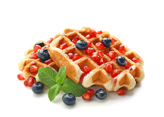 Tasty waffles with berries and pomegranate seeds on white background
