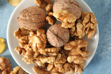 Plate with tasty walnuts on color table, closeup