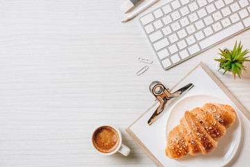 elevated view of clipboard, computer keyboard, croissant and coffee cup at table in office