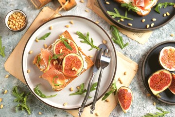 Healthy sandwiches from rye bread with soft cheese, jamon, figs, arugula and pine nuts.