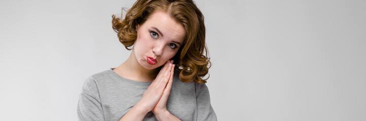 Charming young girl in a gray T-shirt on a gray background. The girl folded her hands together