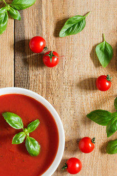 Creamy tomato soup with basil on old wooden kitchen table 