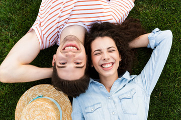 Image from top of joyous couple man and woman 20s, lying alongside opposite heads on green grass in park