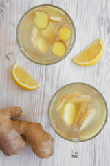 Two mugs of homemade ginger tea with lemon on white wooden table, top view. Flat lay, overhead, from above.