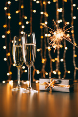 glasses of champagne, present and christmas sparkle on garland light background, christmas concept