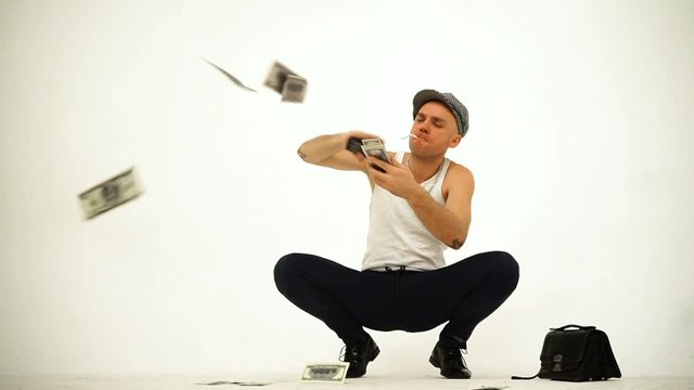 An old fashioned squatting slav in a tank top tweed cap stitting with a leather purse throwing money rain on white background
