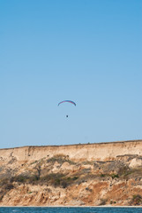 Fototapeta na wymiar Paraglider hovering over the cliff and the landscape of the sea, soaring on the rising air, extreme and entertainment,