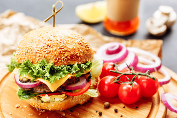 Close-up of home made tasty burgers on wooden table. Decorated with onion, cherry tomatoes and black pepper