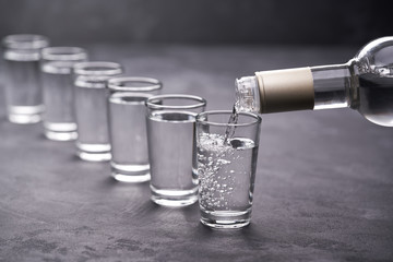 Vodka from the bottle is poured into a glass on a black background, selective focus - obrazy, fototapety, plakaty