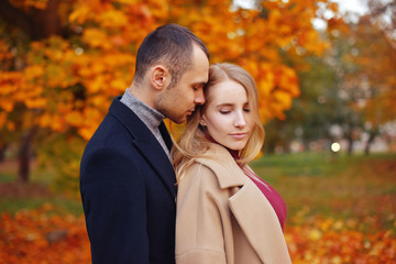 Fototapeta premium Girl and man or lovers on date hug. Couple in love in park . Autumn. Man and woman smile on autumn fallen leaves in a park, enjoying a beautiful autumn day. Young couple in the autumn.