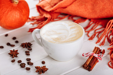 Fototapeta na wymiar Warm knit scarf and cup of hot coffee with foam. Halloween orange pumpkin, spices and other holiday decor. Side view