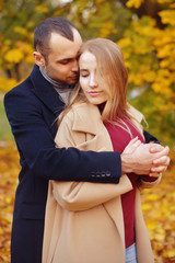 Fototapeta premium Girl and man or lovers on date hug. Couple in love in park . Autumn. Man and woman smile on autumn fallen leaves in a park, enjoying a beautiful autumn day. Young couple in the autumn.