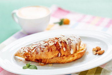 fresh croissants covered with jam and sliced almond on blurred coffe cup background for breakfast