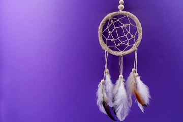 Dream catcher with feathers on purple background.