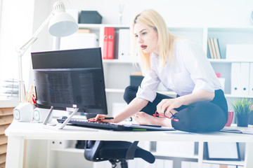 A young girl sitting on a Desk in the office and working with documents and computer.