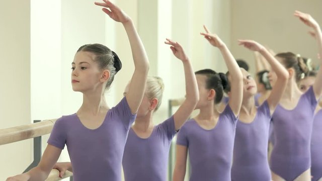 Training of beautiful ballet dancers in studio. Group of ballet girls in purple suits practicing at choreography equipment. Ballet school for teens.