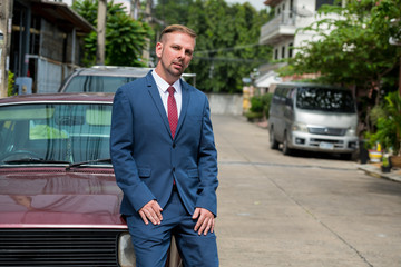 Portrait of blonde businessman leaning on vintage car outdoors
