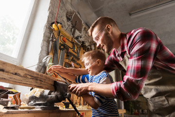 family, carpentry, woodwork and people concept - happy father and little son with rasp grinding...