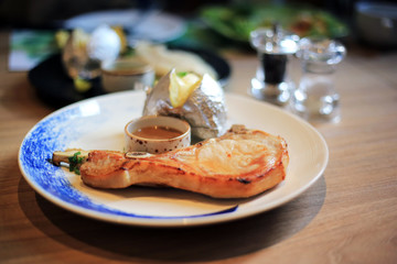 Pork chop steak in dish serve with pepper sauce and baked potato on wood table.